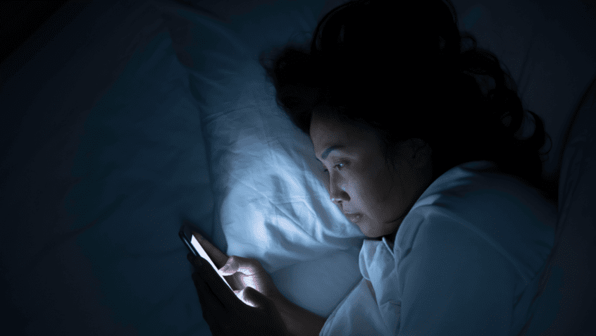 Image of woman looking at her phone while trying to fall asleep